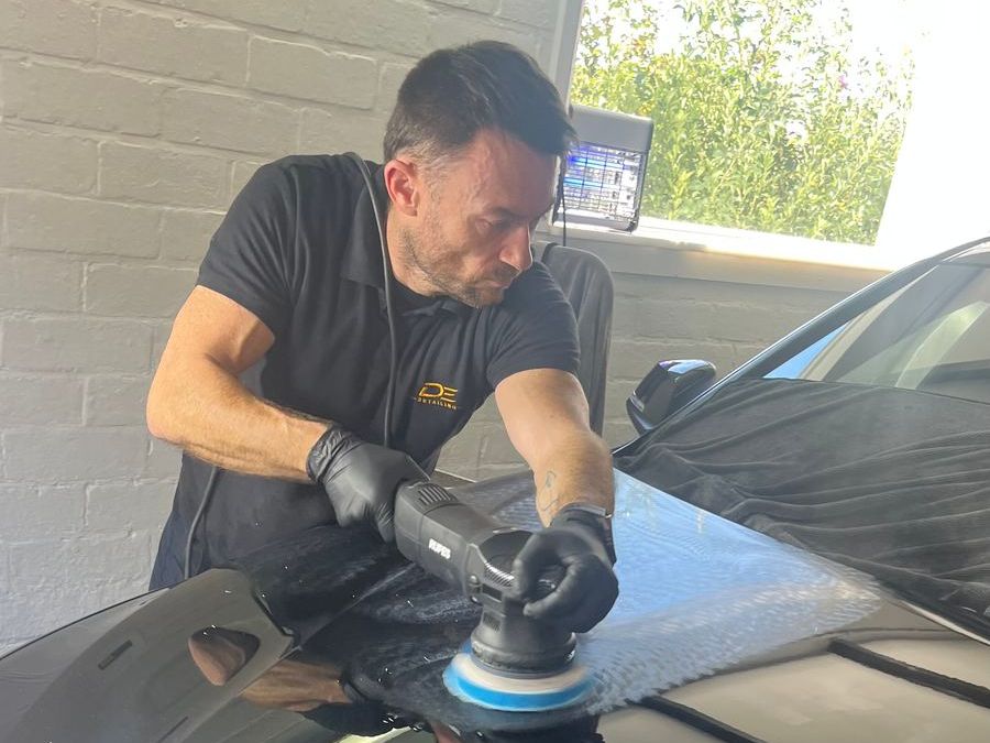 Detailer aan het werk: machinepolijsten van de motorkap van een zwarte BMW